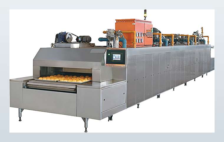 A stainless-steel continuous tunnel oven with trays of baked goods on its conveyor